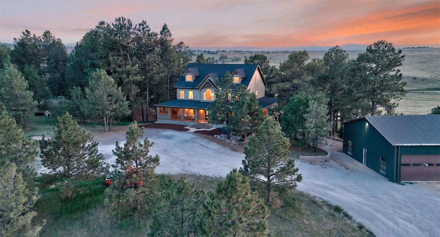 Aerial twilight view of 1516 Bluebird Trail, a Mountain Contemporary estate set among mature ponderosa pines on eight acres in Elizabeth, Colorado, with a detached steel shop